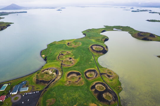 Aerial view of the verdant pseudo craters dotting the landscape contrast starkly with the surrounding serene waters of Skutustadagigar, Lake Myvatn, Iceland.