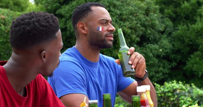 Vertical video: Man in blue tee reacting to offscreen cue at food table, lifting green bottle