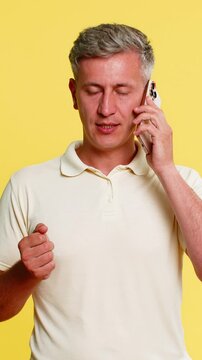 Middle-aged man finishing smartphone call slowly, lowering device with serious face, then sighing deeply as if after hard conversation. Guy expressing emotional fatigue isolated on yellow background.