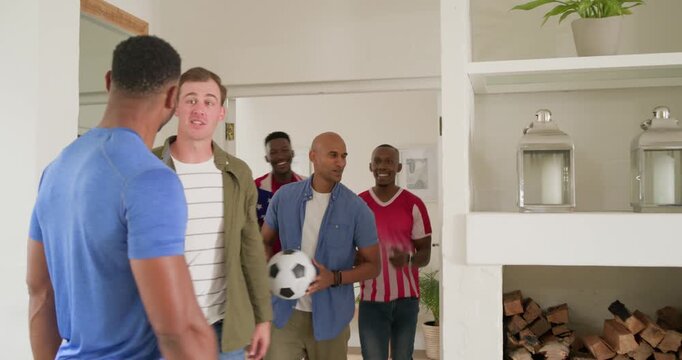 Diverse casual male friends entering home holding soccer ball and sixpack, greeting before game