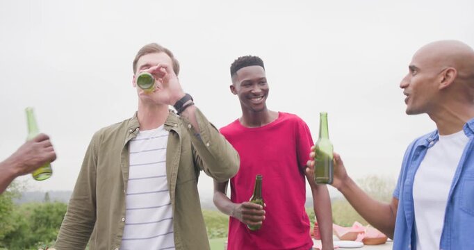Group of four men toasting with green beer bottles celebrating grilling and serving skewers on deck