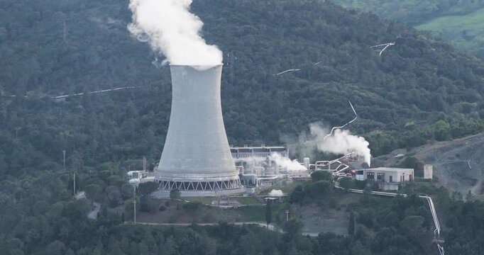 Larderello, Italy - 15 April 2026: Aerial view of Enel Green Power geothermal power plant with a large cooling tower emitting steam amidst the green hills of Tuscany.