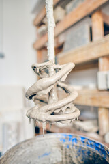 Fototapeta premium Close up of a drill mixer coated in raw gritty wet plaster or cement suspended above a mixing bucket, cool grey slurry dripping from the spiral blade against a soft workshop background,