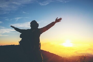 Fototapeta premium Silhouette of Traveler with Backpack Raising Arms at Sunrise on Mountain, Freedom and Adventure Concept, Inspirational Landscape with Golden Light, Travel Lifestyle Success and Achievement Theme