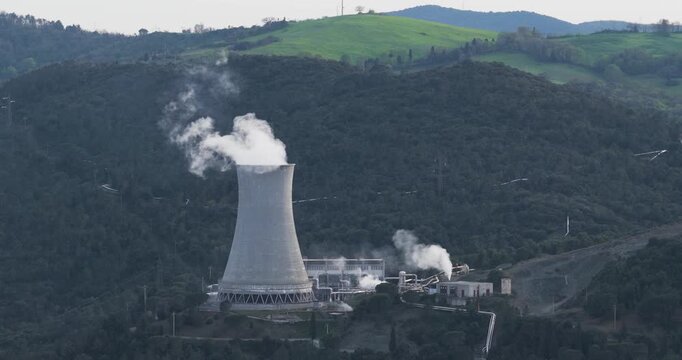 Larderello, Italy - 15 April 2026: Aerial view of Enel Green Power - Centrale Geotermica di Larderello with steam rising from the cooling tower against lush green hills in Tuscany.
