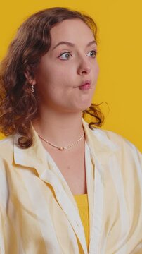 Surprised funny comical playful young woman making fish grimace pout lips, smooching choking, looking with shocked dumb idiotic expression, doing duck face, fooling around. Lady on yellow background