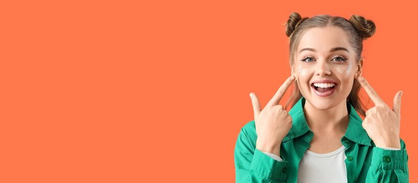 Happy young woman pointing at her creative glitter makeup on orange background with space for text