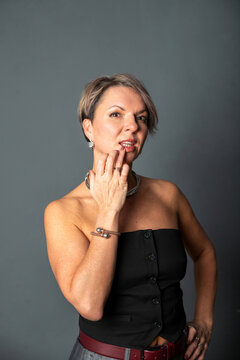 49 year old woman touching her lips with hand. Portrait of a beautiful mature lady in a black top with jewelry. Elegant female model with short hair expressing feminine confidence.