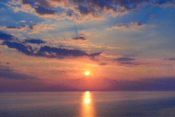 Obraz premium Sunset over ocean horizon with glowing sun and purple clouds in the sky, concept of peace and inspiration