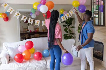Naklejka premium African American couple decorating living room with colorful latex balloons and Birthday banner