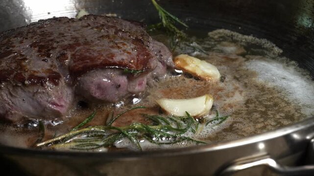 Thick ribeye steak bastes in butter with garlic and rosemary