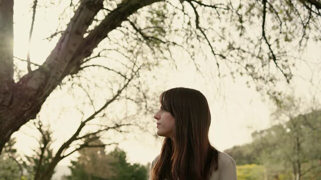 Thoughtful young woman walking alone in a park during a beautiful spring sunset