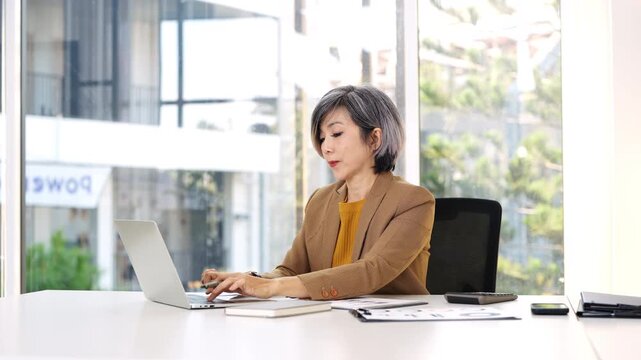 mature middle aged professional business woman manager executive wearing suit looking at laptop computer in office working at desk.