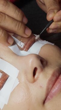 Woman undergoing an eyelash lift procedure, featuring a close up view of a beauty technician carefully applying an enhancing solution to her natural lashes for a professional lash perm