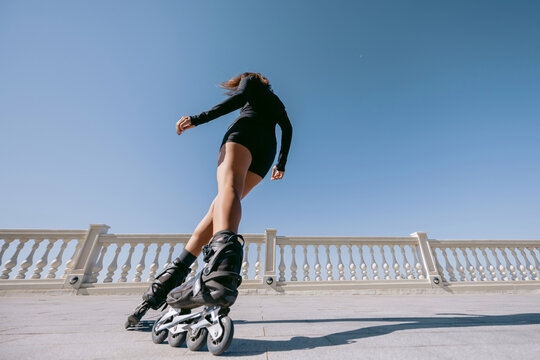 Low angle view of woman rollerblading under blue sky, dynamic summer action shot.