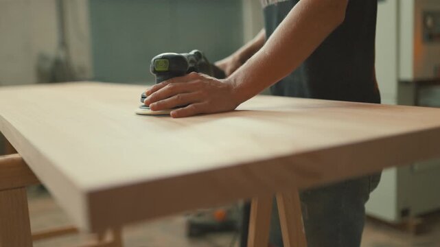 Woodworker hands sanding wooden plank with orbital sander