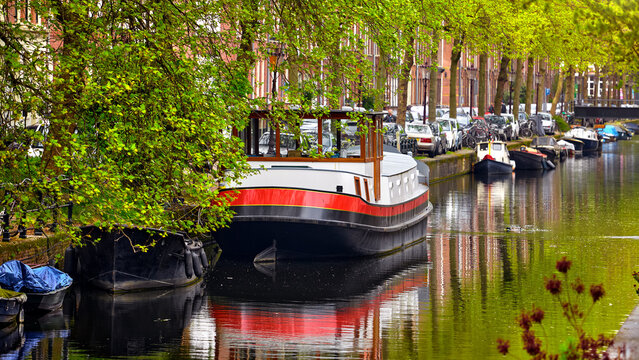Netherlands Amsterdam. View at river Amstel with traditional houses at bank and boats at water canal. Scenic cityscape. Spring day.