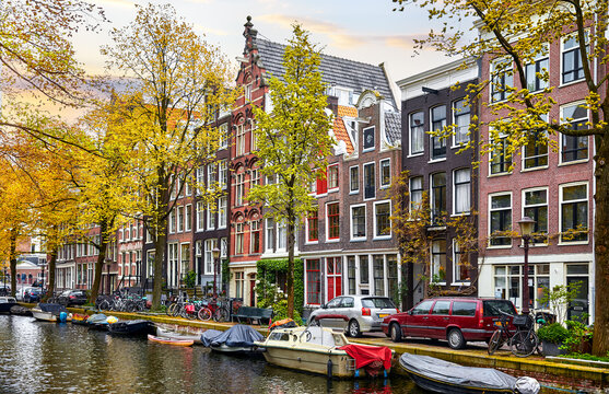 Amsterdam, Netherlands. Panorama of famous dancing houses on river Amstel, water channels with house boats. Popular landmark and travel destination in old european city. Evening sunset landscape.
