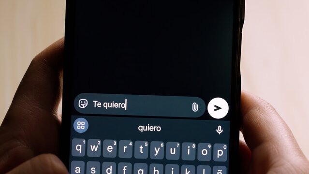 Close-up of hands holding a smartphone while typing "Te quiero!" (I Love You!)