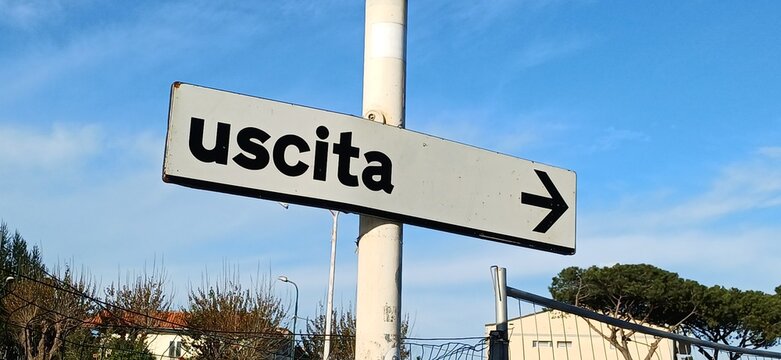 Wei&szlig;es Wegweiserschild mit der italienischen Aufschrift Uscita und einem Pfeil nach rechts vor blauem Himmel