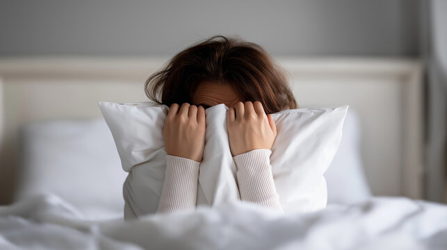 Person hiding face in pillow while lying in bed, symbolizing reluctance to wake up and morning fatigue.