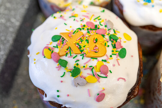 Close-up of traditional Ukrainian Easter bread paska with white icing, colorful sprinkles and golden XB letters symbolizing Christ is risen. Festive holiday dessert, shallow depth of field.