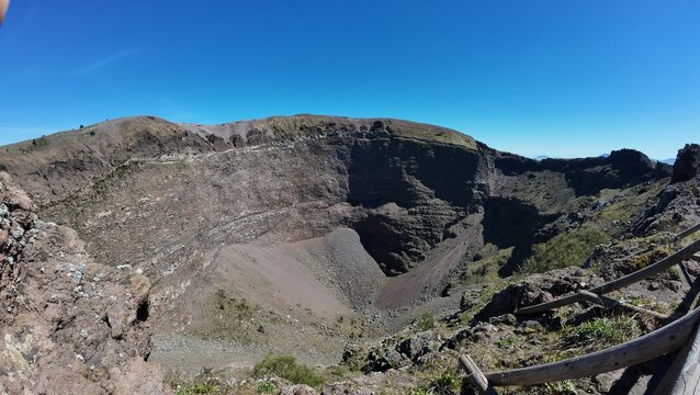 Blick in den tiefen Krater des Vesuvs mit seinen steilen Aschew&auml;nden und Vulkangestein unter strahlend blauem Himmel