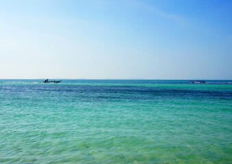 Fototapeta premium Fast motorboat carries tourists across ocean. Boat moves sea on sunny day near coastline in tropical island. Boat travels through clear blue sea water under bright sky. Traveling on sea in Vietnam. 