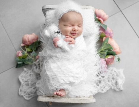Newborn Baby Girl Smiling And Sleeping In A Crib With Flowers During A Photoshoot