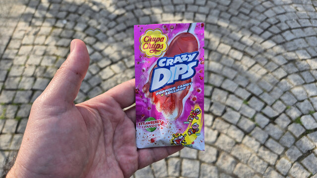 A hand holds a pink packet of Chupa Chups Crazy Dips strawberry flavored popping candy and lollipop against a blurred cobblestone background. Picture taken on April 15, 2026 in Bucharest, Romania.
