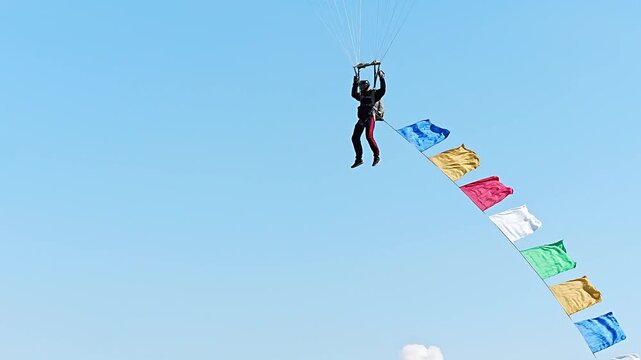 Skydiver Under Parachute with Colorful Flags Against Clear Blue Sky