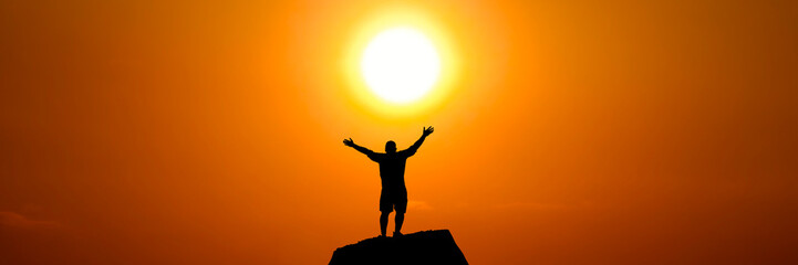A silhouette of person stands with open arms as the sun rises © Stock4u2024 