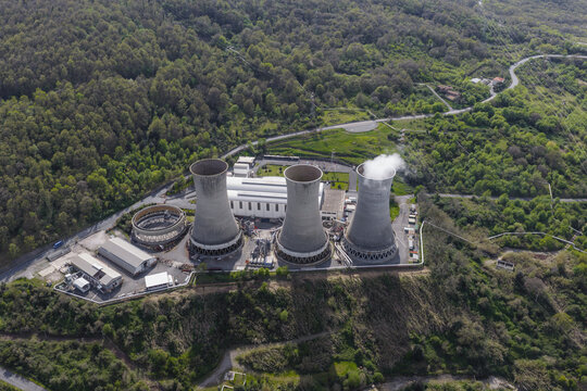 Larderello, Italy - 10 April 2026: Aerial view of Enel Green Power - Centrale Geotermica di Larderello geothermal power plant with cooling towers and steam surrounded by lush green hills.
