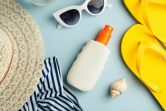 Sunscreen bottle and beach accessories. Summer travel holiday concept. Blue background flat lay. Top view