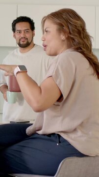 Vertical video: Starting chat, seated woman holding mug, gesturing and making point at home kitchen