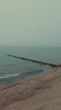 Wooden groynes and large rocks on the seashore. Coastal landscape with rough waves hitting barrier structures. Minimalist marine scenery for nature background.