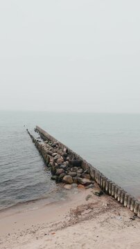 Wooden groynes and large rocks on the seashore. Coastal landscape with rough waves hitting barrier structures. Minimalist marine scenery for nature background.