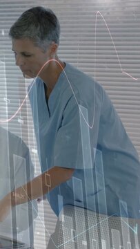 Vertical video: Nurse leaning over tablet, pointing as health graphs showing, doctor watching scope