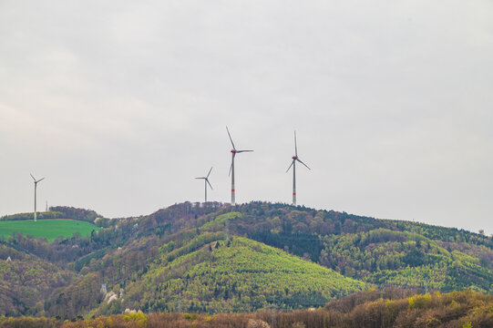Wind turbines stand tall on rolling green hills under a cloudy sky