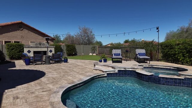 A 4k aerial view of a desert landscaped home in Arizona featuring a travertine tiled pool deck with a fireplace and outdoor kitchen.