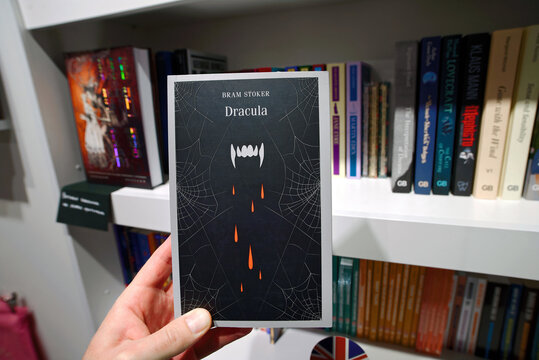 Minsk, Belarus. Apr 12, 2026. Book Dracula by Bram Stoker. Hand holding Bram Stoker's classic gothic horror novel Dracula with striking black cover featuring vampire fangs and spider webs in bookstore