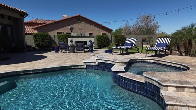 A 4k aerial view of a desert landscaped home in Arizona featuring a travertine tiled pool deck with a fireplace and outdoor kitchen.