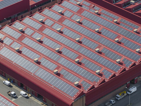 Larderello, Italy - 10 April 2026: Aerial view of Enel Green Power - Centrale Geotermica di Larderello with solar panels on red industrial rooftops and parked service vehicles.