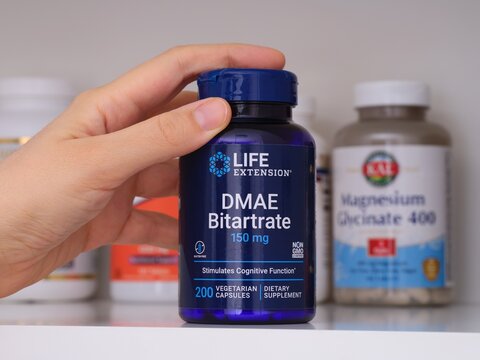 Tambov, Russian Federation - February 19, 2022 Woman taking blue bottle of Life Extension DMAE Bitartrate capsules out of shelf with other supplement jars. Close-up