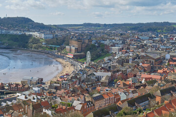 Obraz premium An elevated view of Whitby, North Yorkshire, showing a curved sandy beach, numerous buildings, and a Ferris wheel. Hills rise in the background in Scarborough - Yorkshire - Great Britain