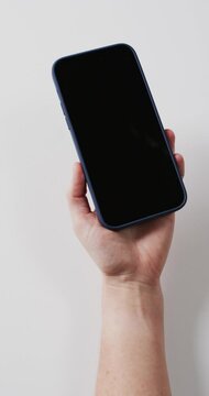 Vertical video: Right hand is lifting phone from lower right to center rotating upright before wall