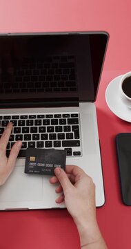 Vertical video: Right hand bringing credit card over laptop as left hand typing to enter payment