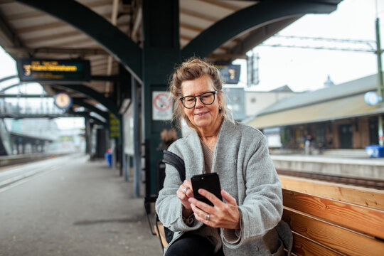 Senior woman using smartphone at train station bench