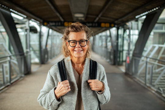Smiling senior woman with backpack on train station footbridge