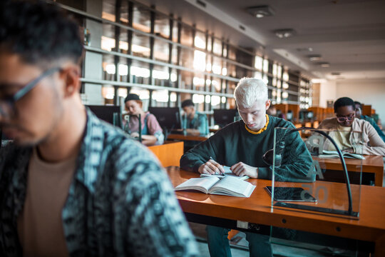 Students studying and taking notes in university library reading room